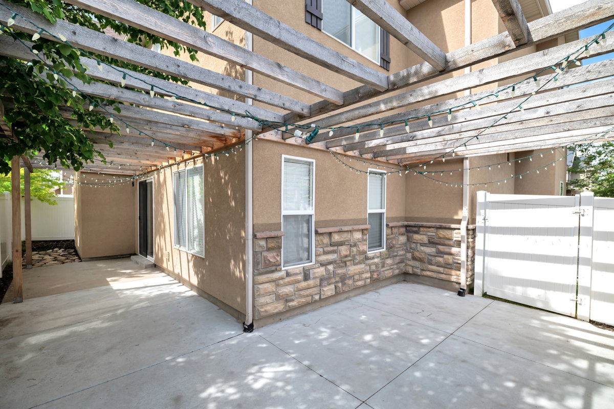 Pergola-covered patio featuring a concrete surface, a stucco exterior, stone accent siding, a sliding glass door, and white privacy fencing
