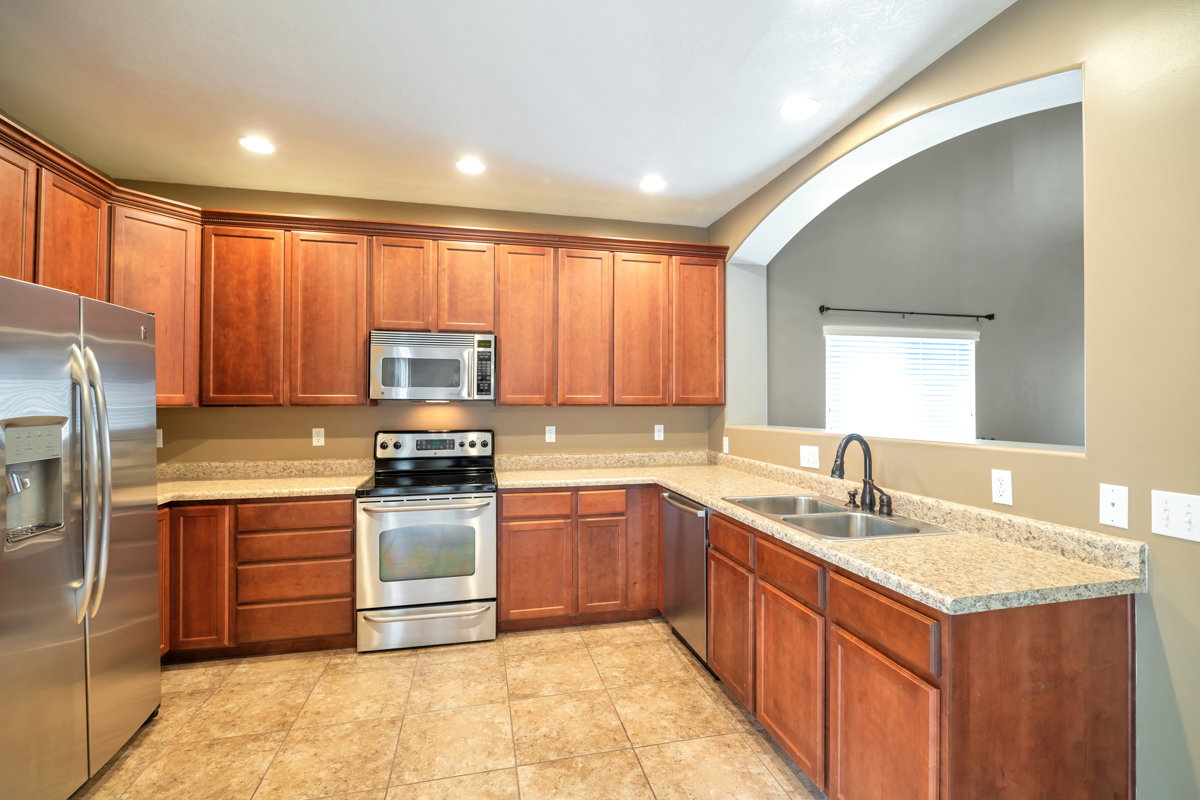 Kitchen featuring extensive wood cabinetry, stainless steel appliances, speckled countertops, a double basin sink with a high-arc faucet, and tiled flooring