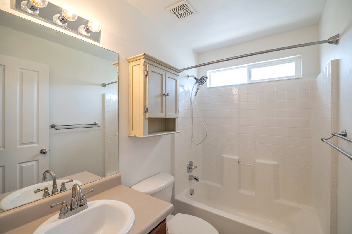 Bathroom featuring a vanity with an integrated sink, a large wall-mounted mirror, overhead lighting, a built-in storage cabinet, and a bathtub with white subway tile surround and an upper window