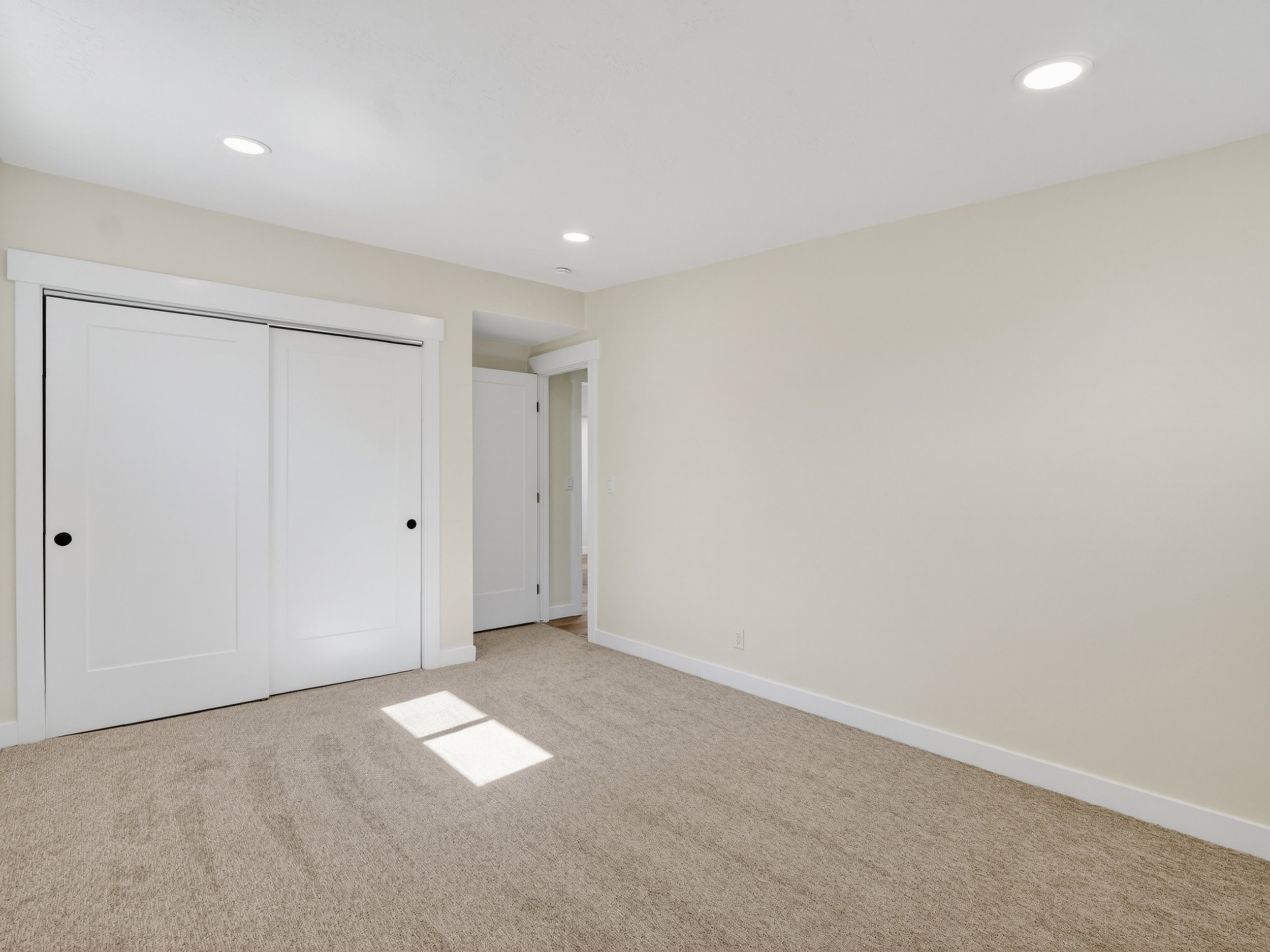 Carpeted interior space featuring a double sliding closet door with black hardware, recessed ceiling lighting, and light neutral wall paint