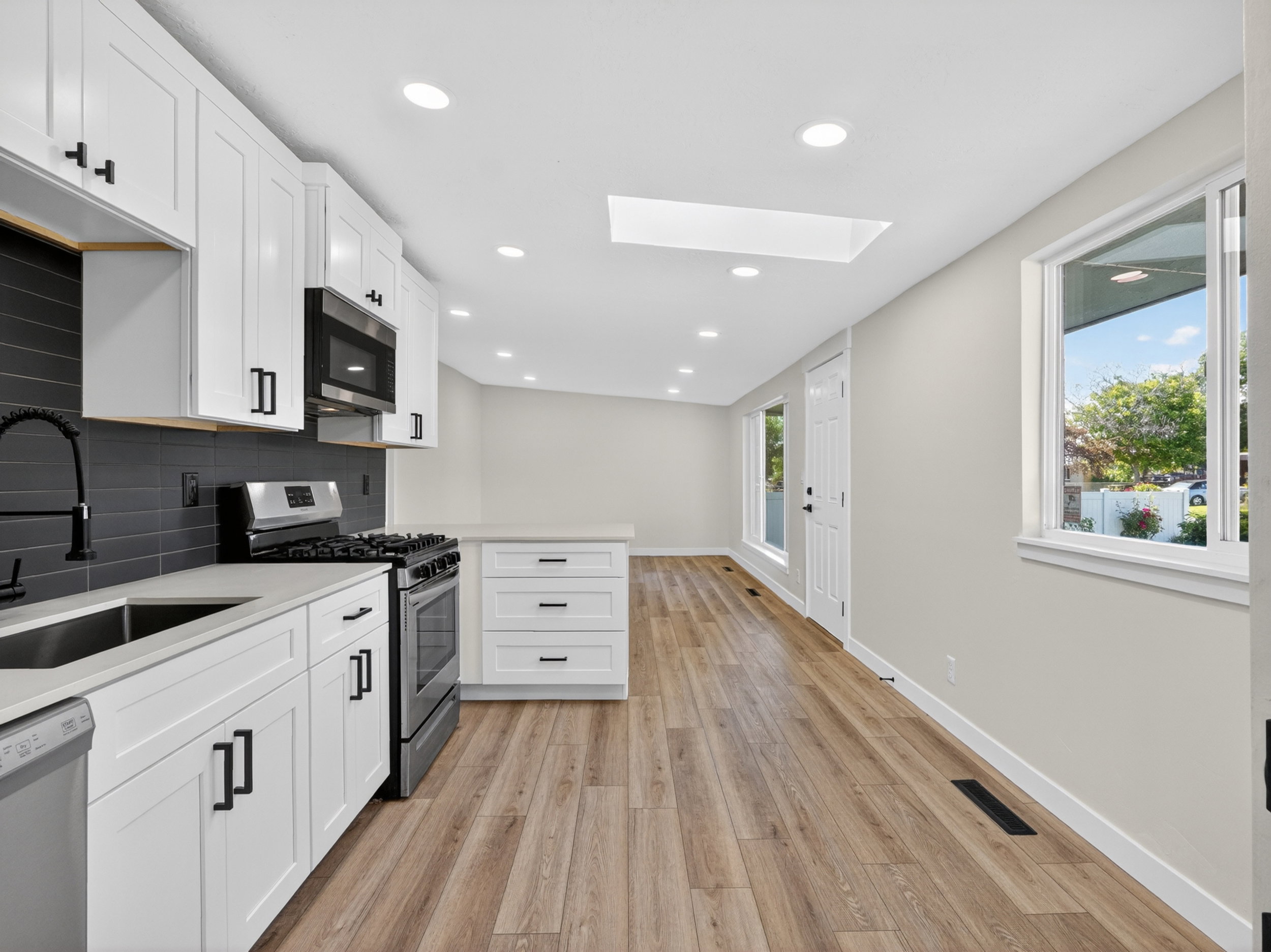 Contemporary kitchen featuring white cabinetry, black hardware, stainless steel appliances, and wood-finish flooring