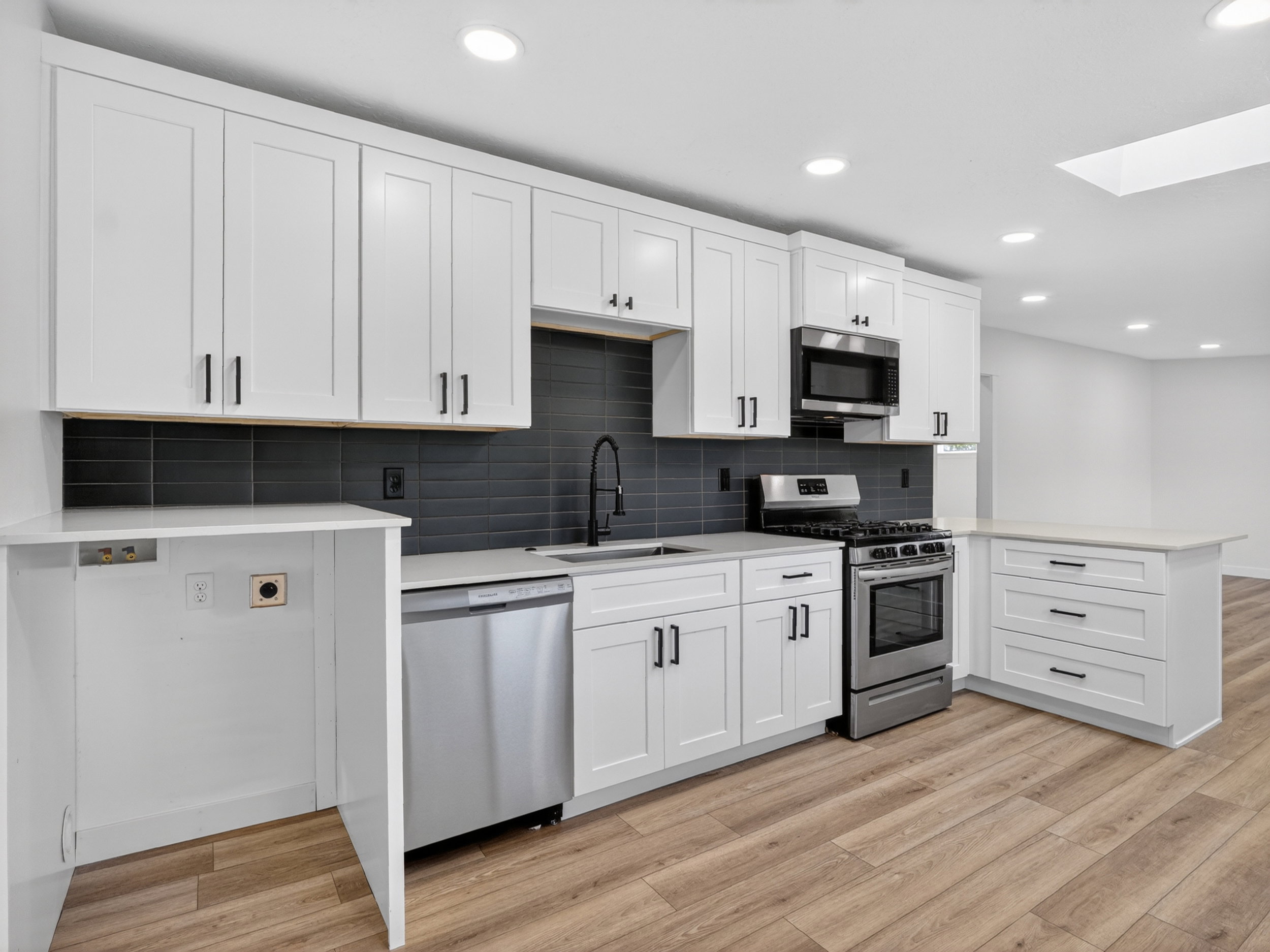 Modern kitchen featuring white cabinetry, stainless steel appliances, a dark subway tile backsplash, light countertops, and wood-finish flooring