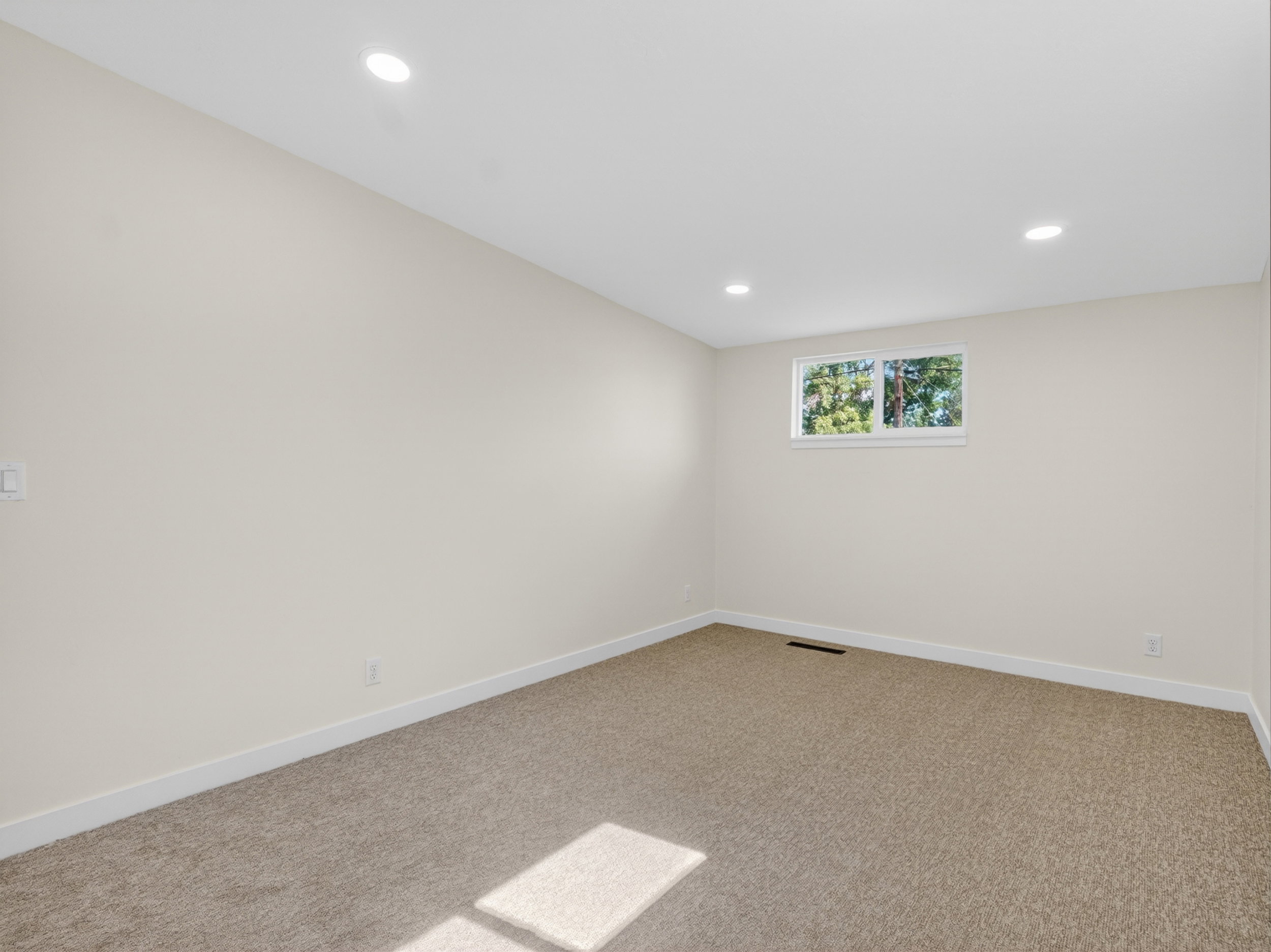 Spacious room with plush carpet flooring, recessed lighting, white trim, and a window providing natural illumination