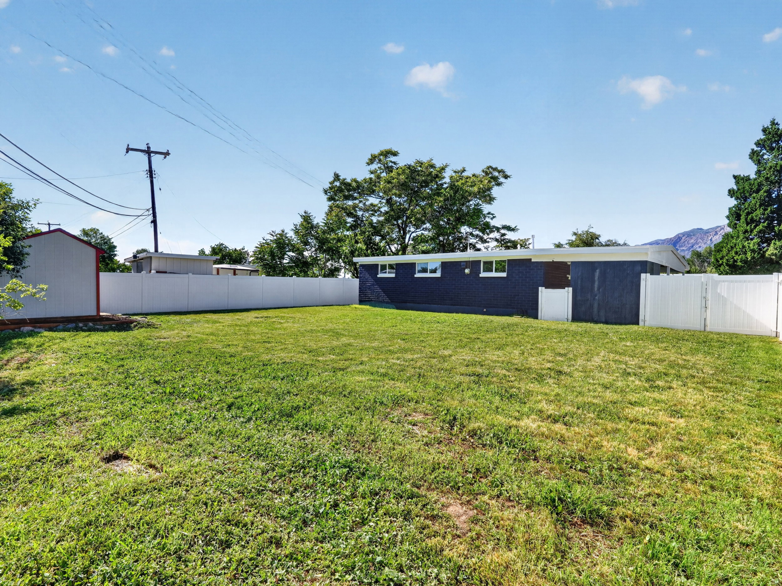 Expansive grass lawn featuring full perimeter white fencing, a detached storage shed, and a dark-colored exterior structure with white trim windows