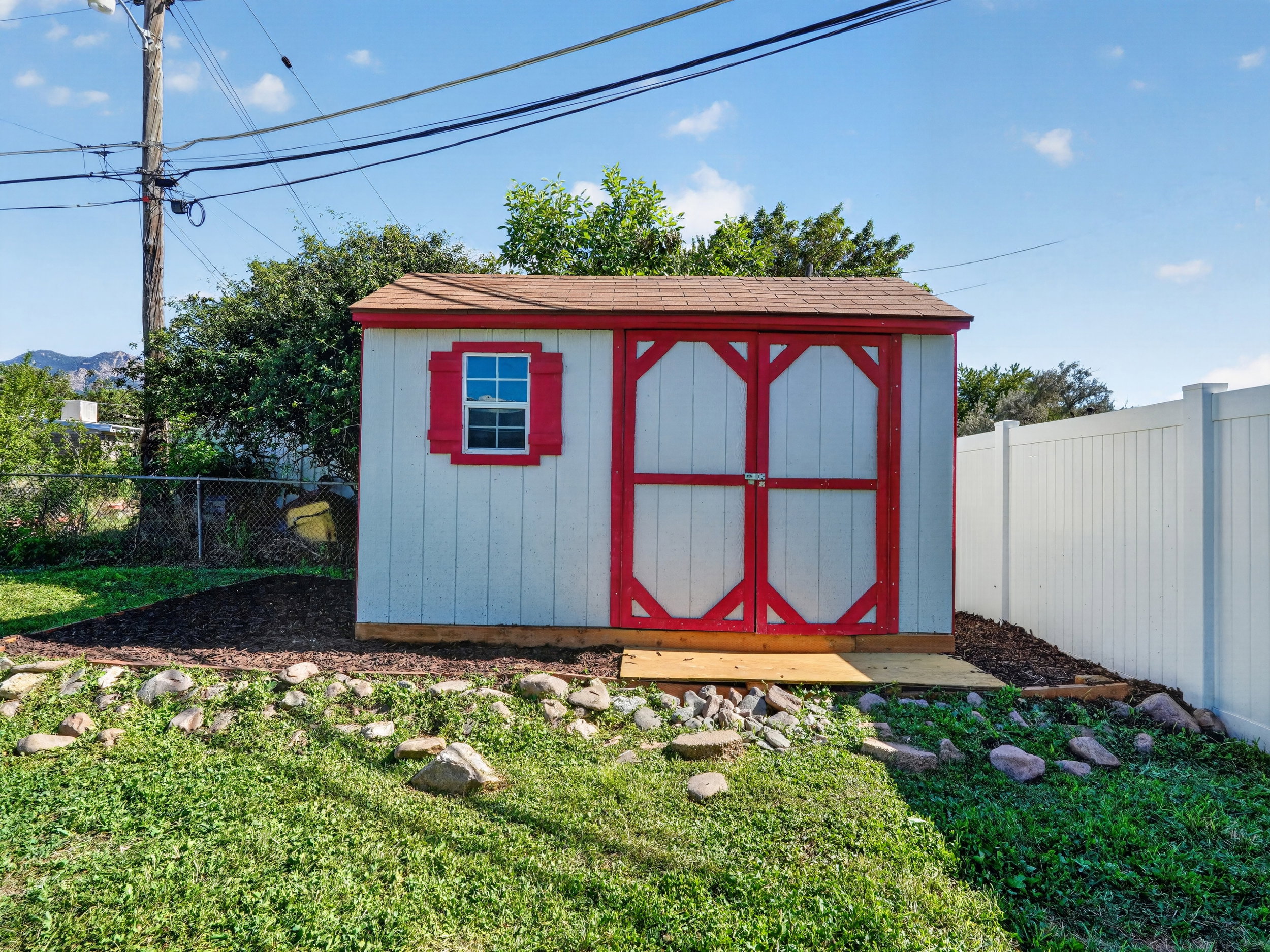 Detached storage shed featuring white siding with red trim accents, a single window, and double entry doors