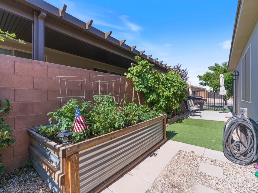 Backyard featuring a wood and corrugated metal raised garden bed, privacy wall, artificial turf, and paved patio area