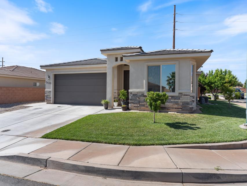 Modern stucco exterior with stone accents, featuring a two-car garage, a concrete driveway, and a manicured front lawn