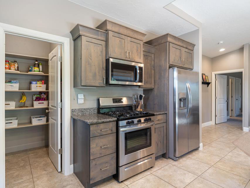 Kitchen featuring stainless steel appliances, stone-finish countertops, wood-finish cabinetry, and a walk-in pantry with shelving