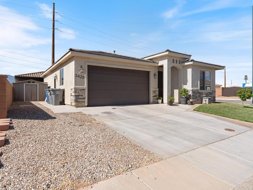 Stucco exterior featuring stacked stone accents, an attached garage, a concrete driveway, and a gravel side yard