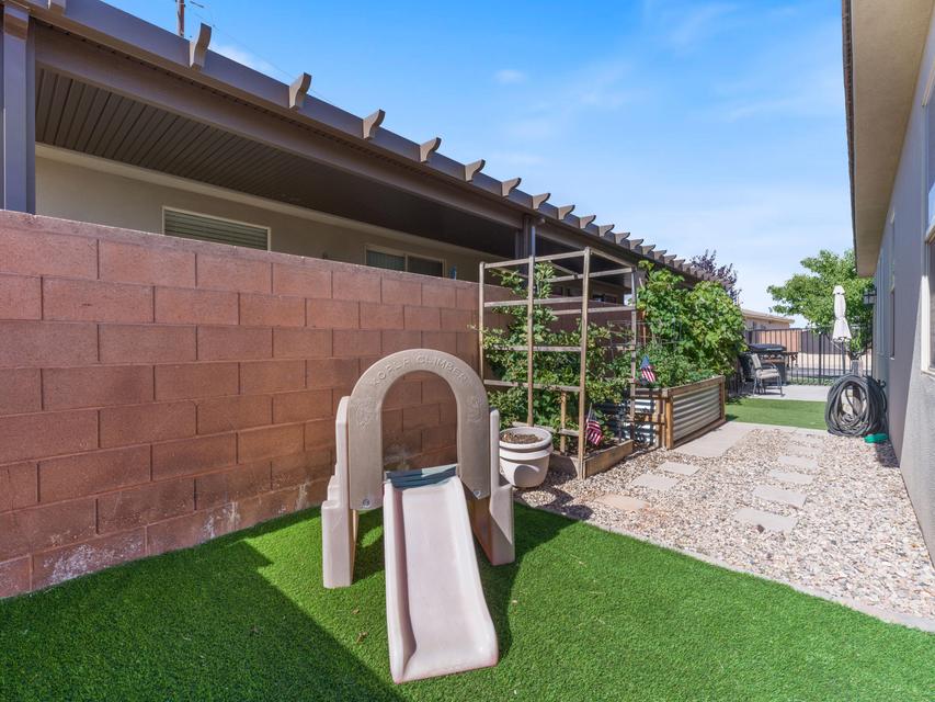 Outdoor space featuring synthetic turf, stone paver pathway, gravel landscaping, and a red brick wall