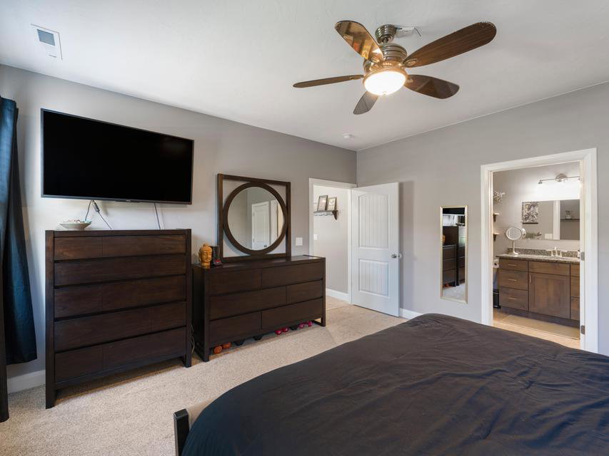 Carpeted bedroom featuring a ceiling fan with integrated lighting, light gray wall paint, and a doorway opening to a bathroom