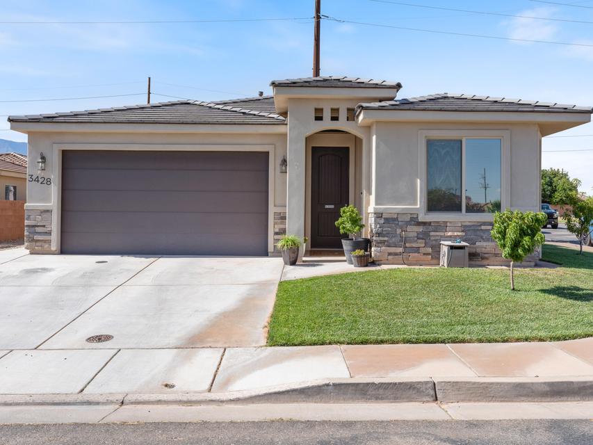 Exterior featuring stucco siding, stone accents, a dark wood entry door, and a two-car garage with a concrete driveway