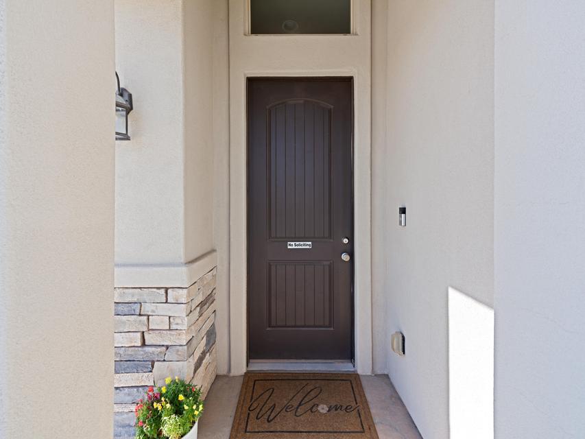 Entryway featuring a dark paneled door with transom window, stucco siding, stone accents, and an outdoor wall lantern