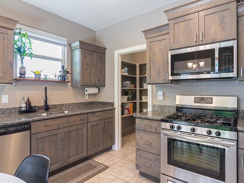 Kitchen featuring gray-toned wood cabinetry, granite countertops, and stainless steel appliances including a gas range and built-in microwave