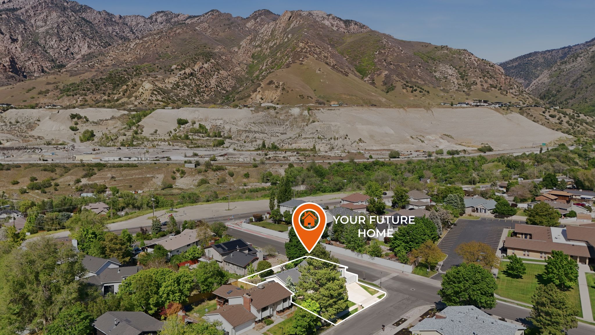 Aerial perspective showcasing a residential property with a highlighted perimeter, situated within a neighborhood featuring mature trees and mountain backdrops
