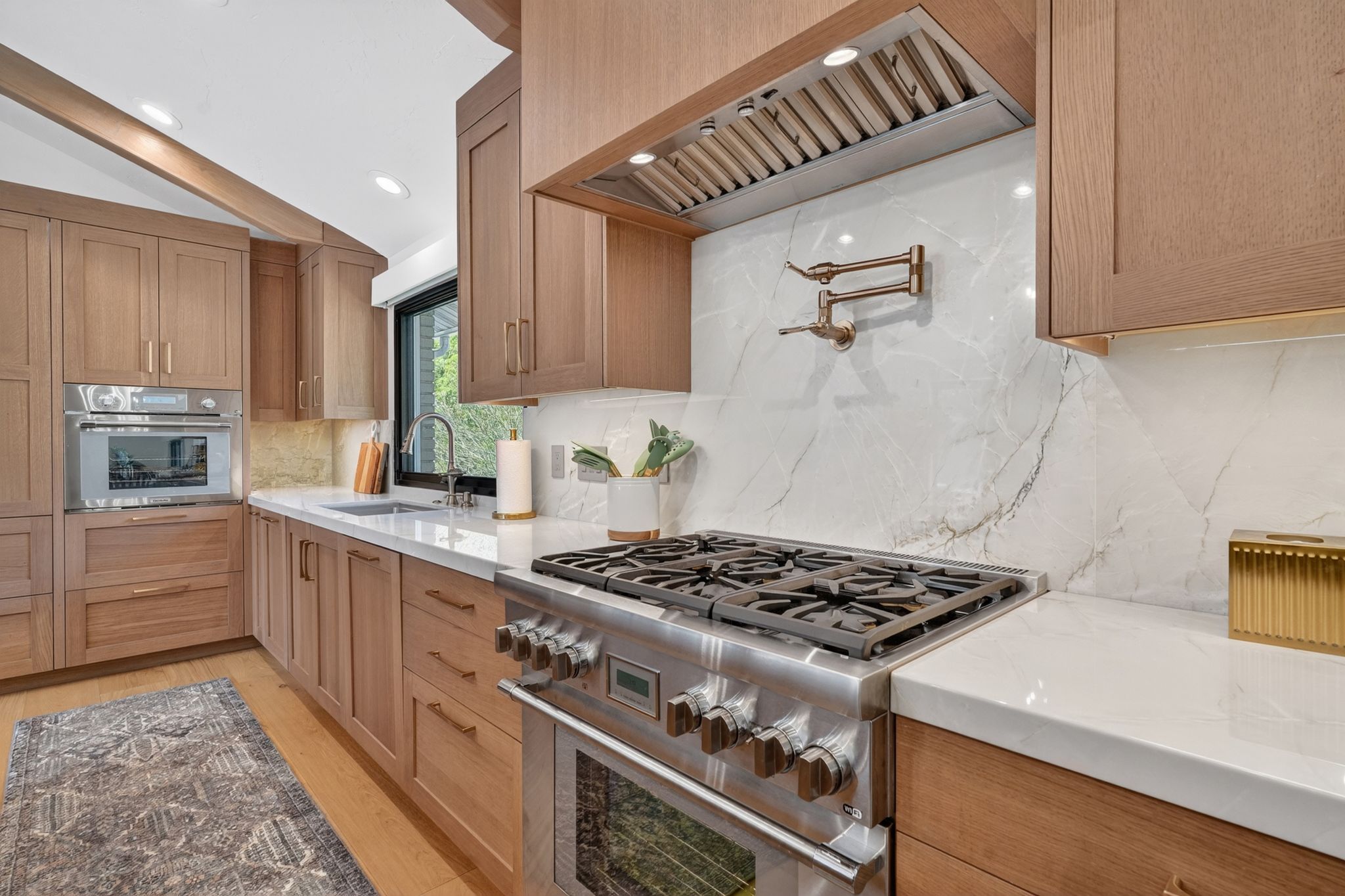 Gourmet kitchen featuring a professional-grade gas range, full-height  backsplash, light wood-finish cabinetry, built-in wall oven, and undermount stainless steel sink