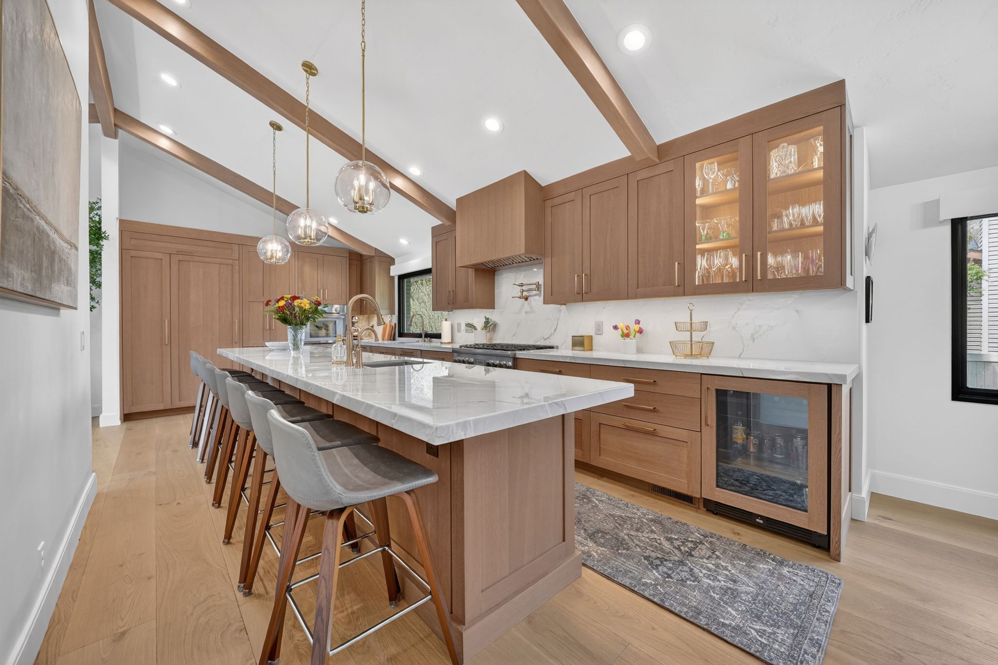 Modern kitchen featuring a vaulted ceiling with exposed wood beams, light wood-finish flooring, and a substantial island with seating