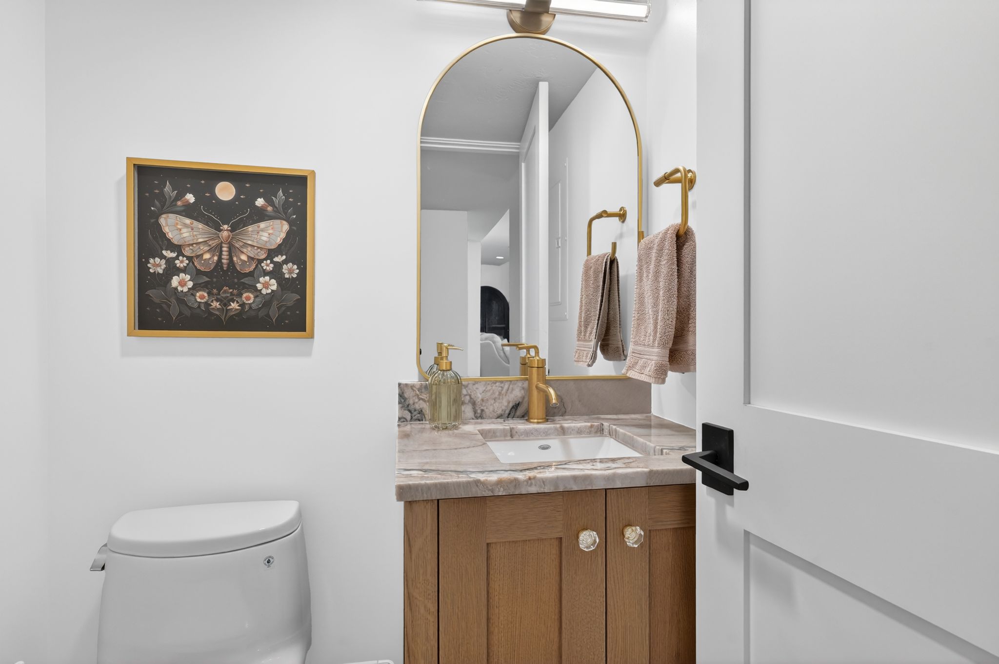 Bathroom vanity featuring a vessel sink, brass faucet, and arched mirror