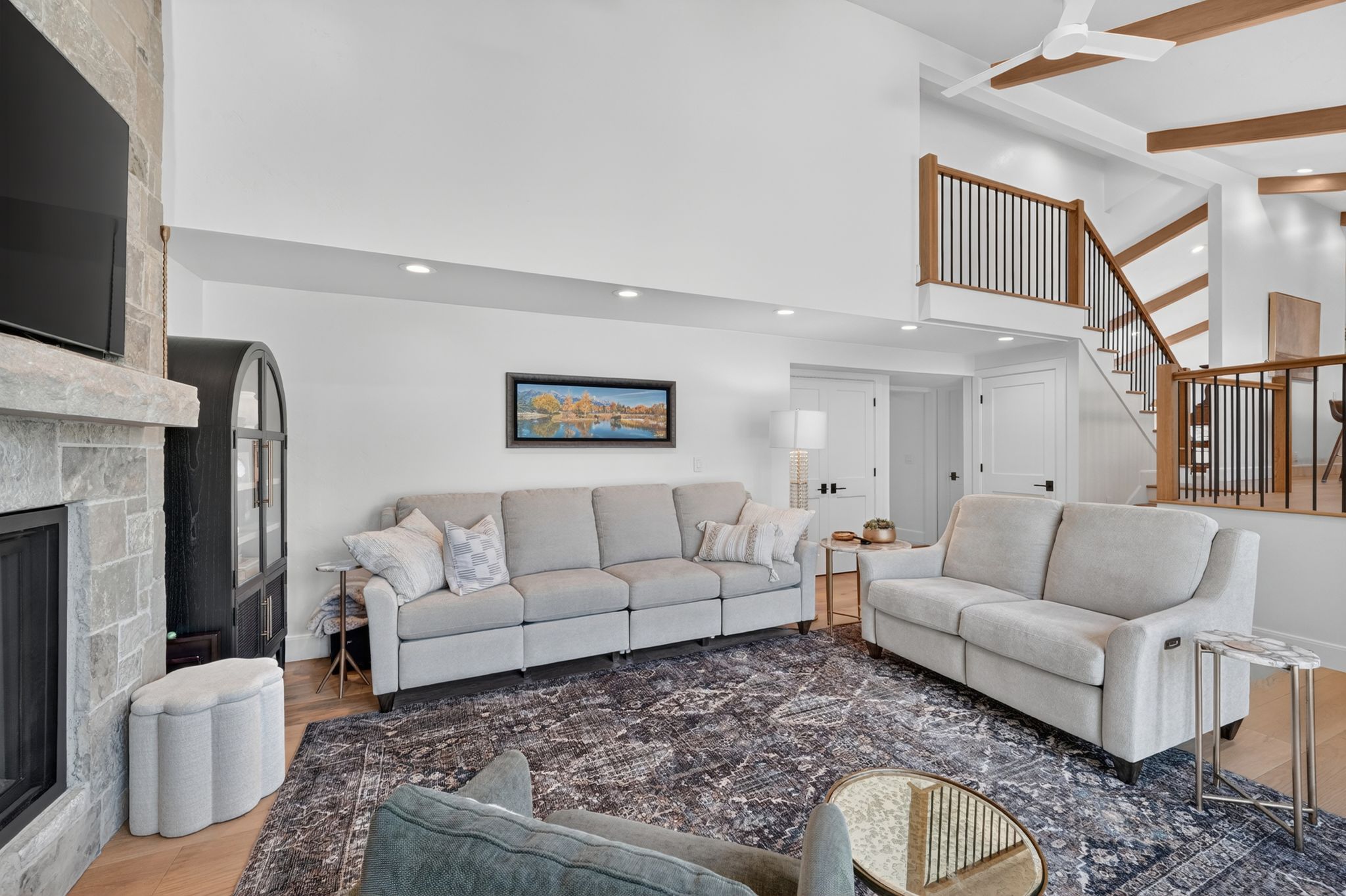 Spacious living area featuring a stone-clad fireplace, wood-finish flooring, recessed lighting, and a multi-level staircase with wood and metal railing