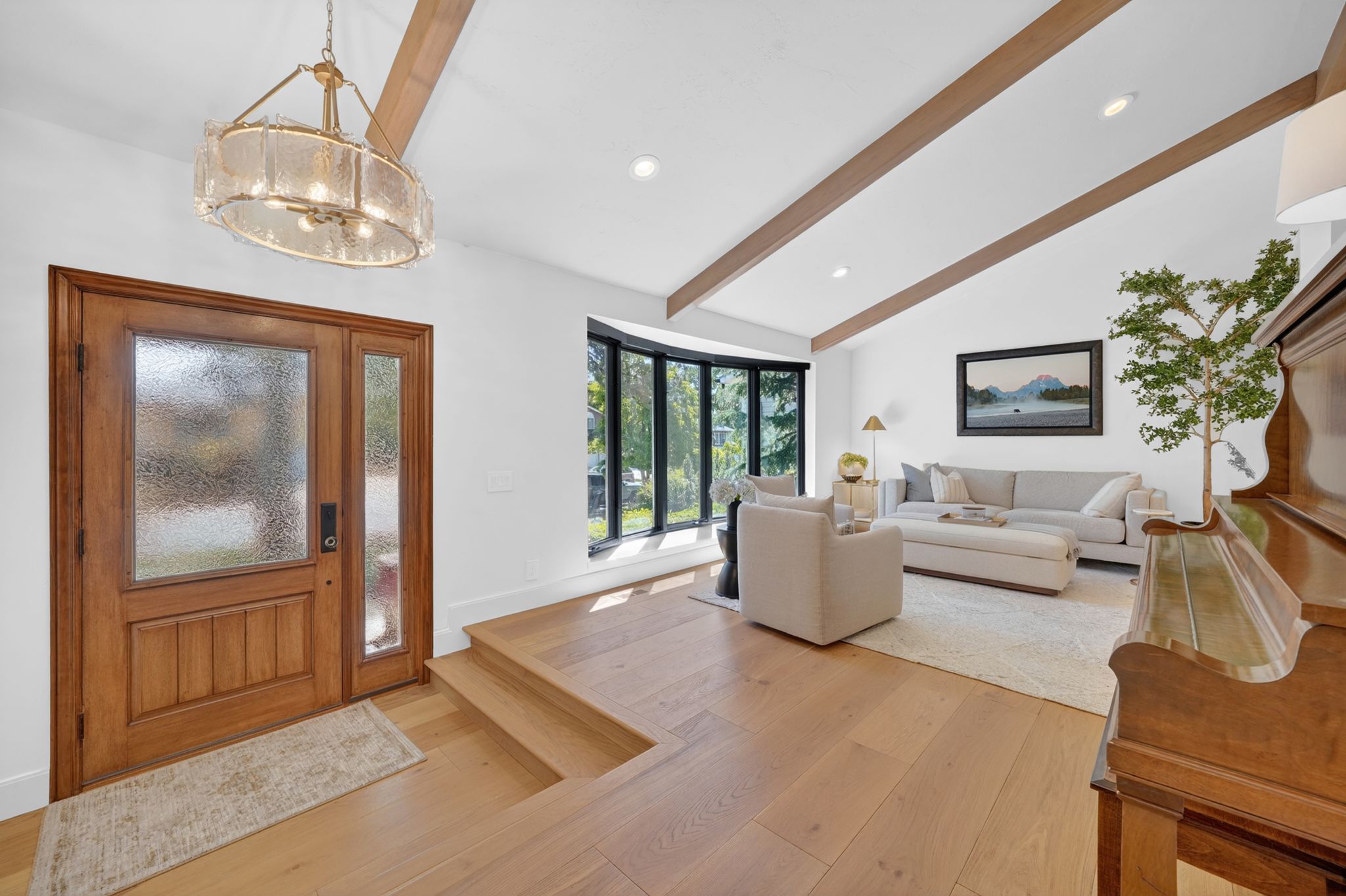 Vaulted ceiling with exposed wood beams, natural wood-finish flooring, and a large bay window