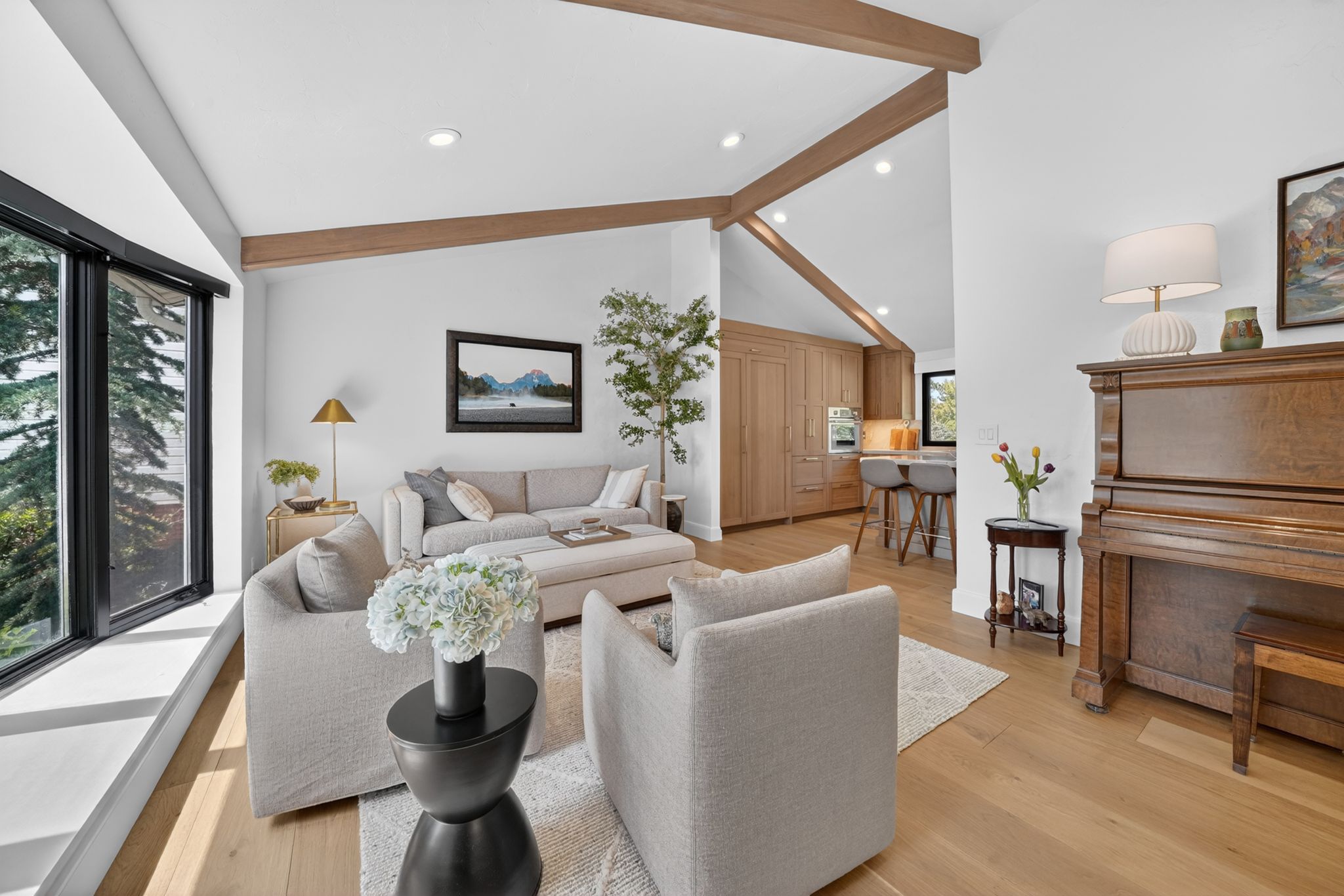 Open-concept living area featuring vaulted ceilings with exposed wood beams, expansive windows with black frames, recessed lighting, and wood-finish flooring