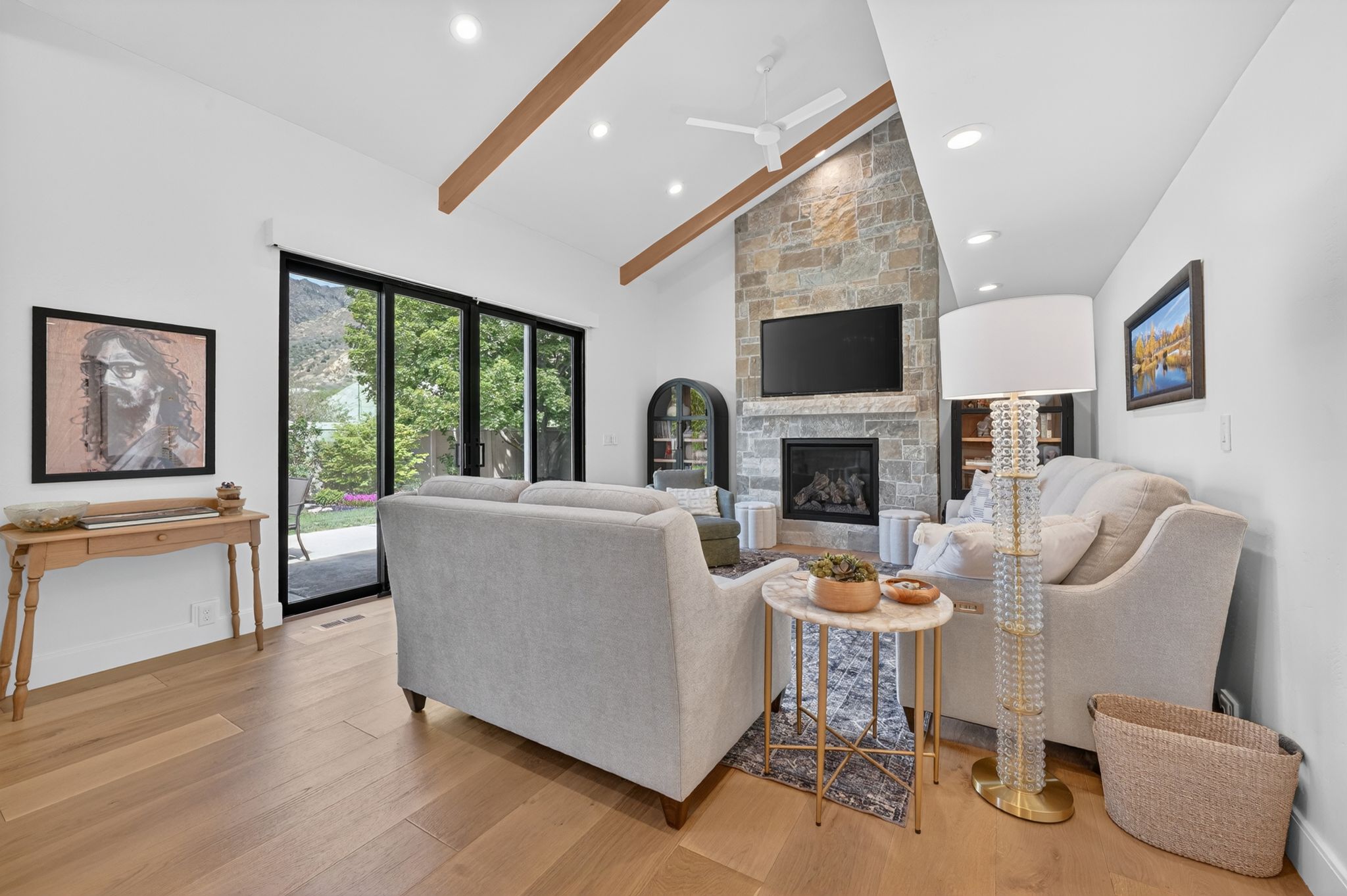 Living area featuring a stone fireplace with hearth, wood-finish flooring, vaulted ceilings with exposed beams, and recessed lighting