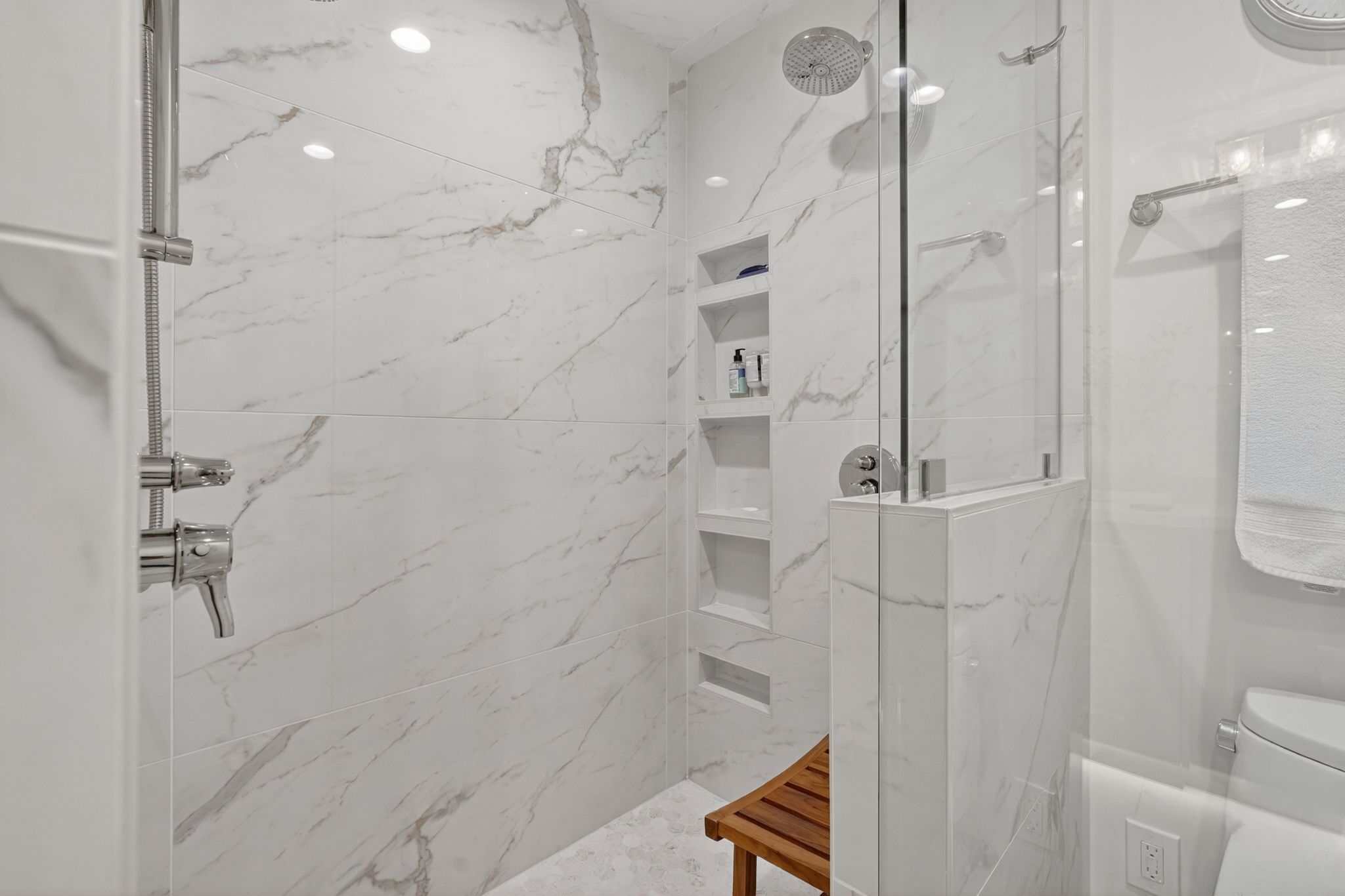 Spacious shower featuring full-height marble tile, a rain showerhead, built-in recessed shelving, a glass enclosure, and a chrome shower system
