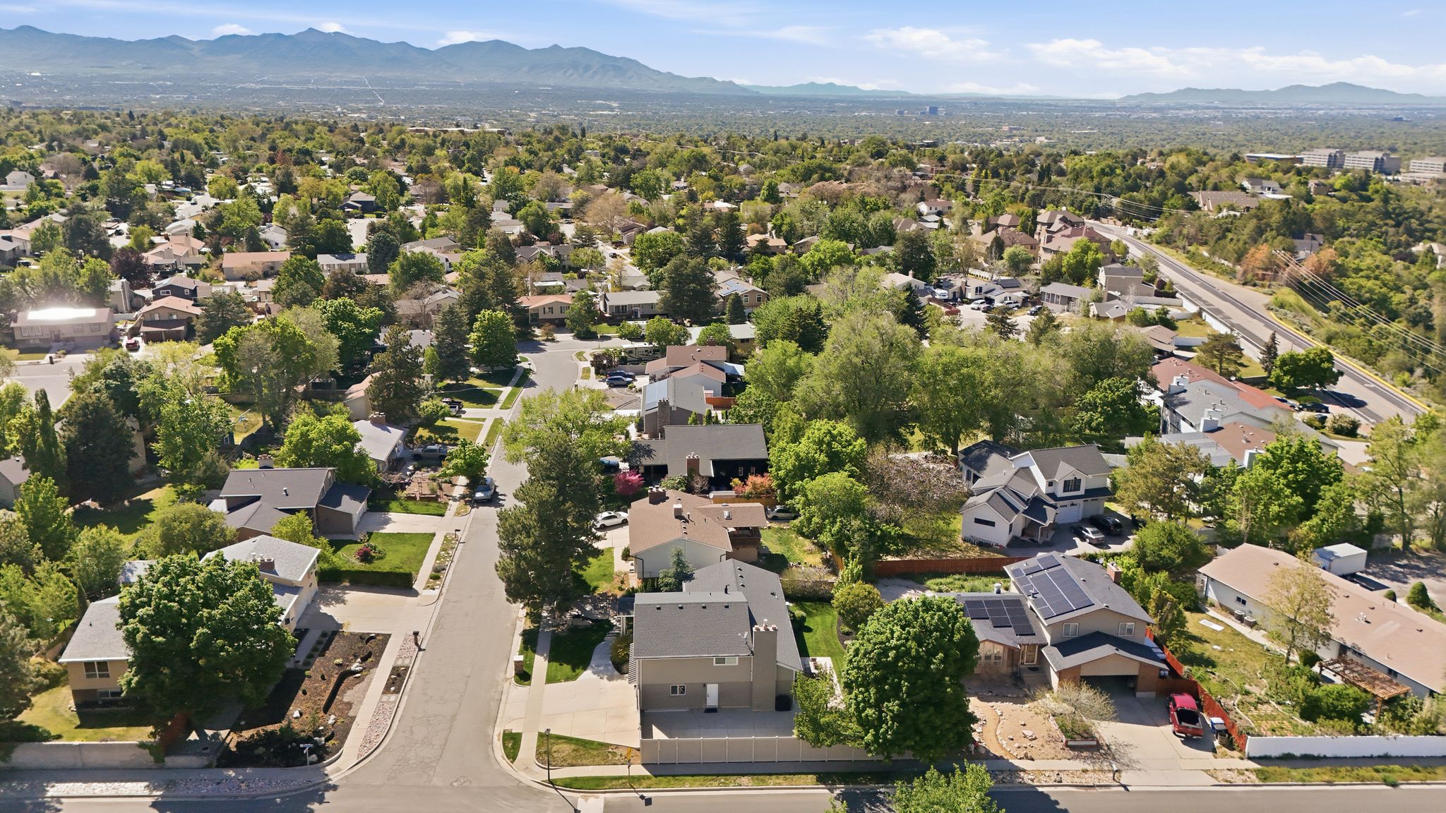 Aerial perspective showcasing a residential area with mature trees and mountain ranges in the distance