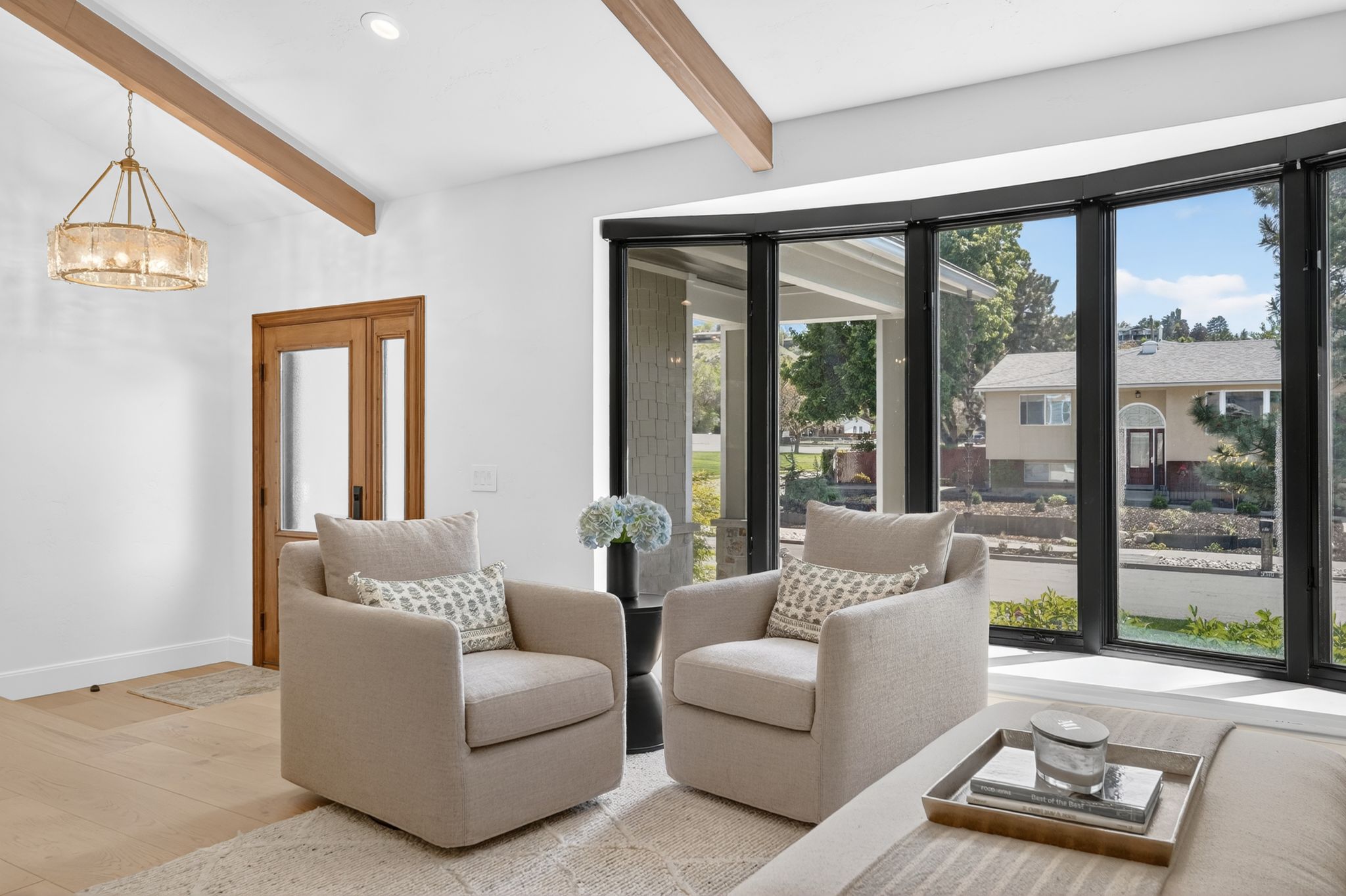 Curved window wall with black framing, wood-finish flooring, exposed ceiling beams, recessed lighting, and a decorative chandelier