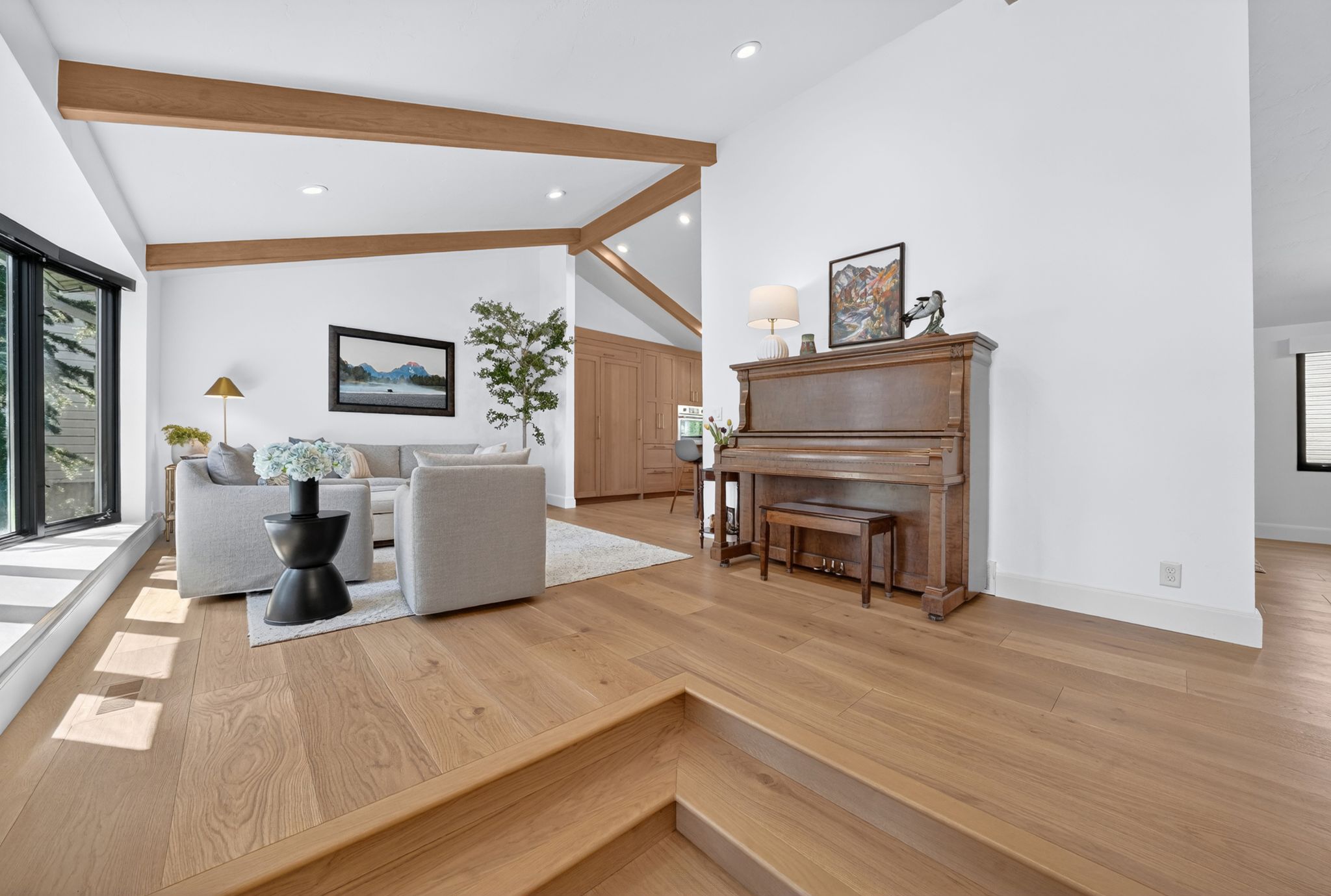 Spacious living area featuring light wood-finish flooring, vaulted ceilings with exposed wood beams, and recessed lighting