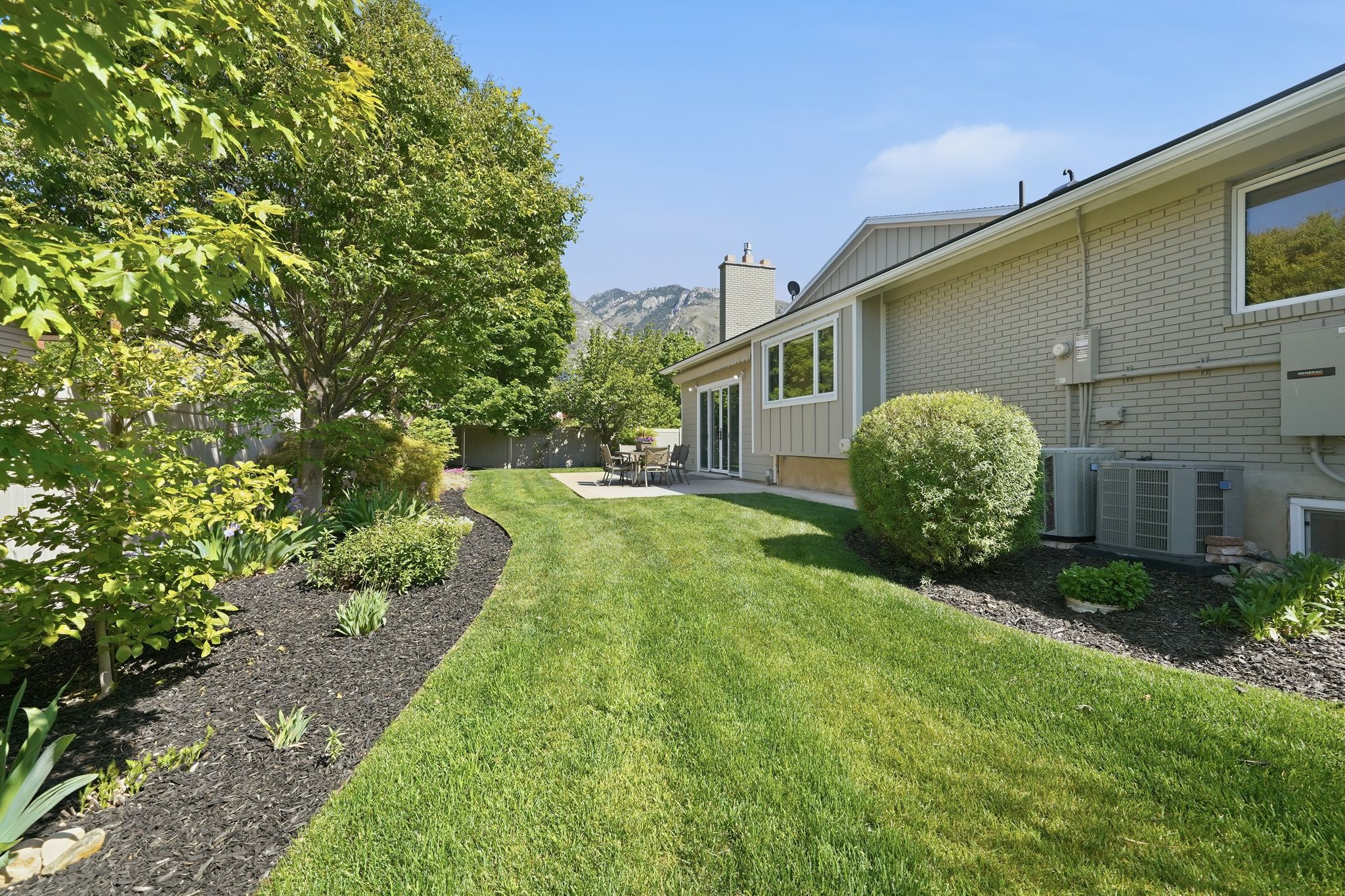 Expansive green lawn with mature trees and landscaped beds featuring black mulch