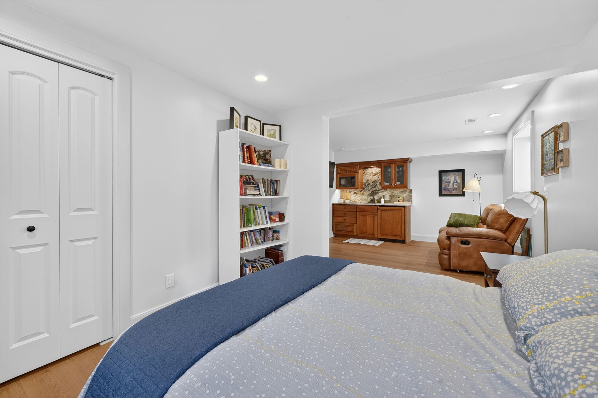 Basement bedroom Open-concept living area featuring wood-finish flooring, a built-in wet bar with wood cabinetry and stone backsplash, recessed lighting