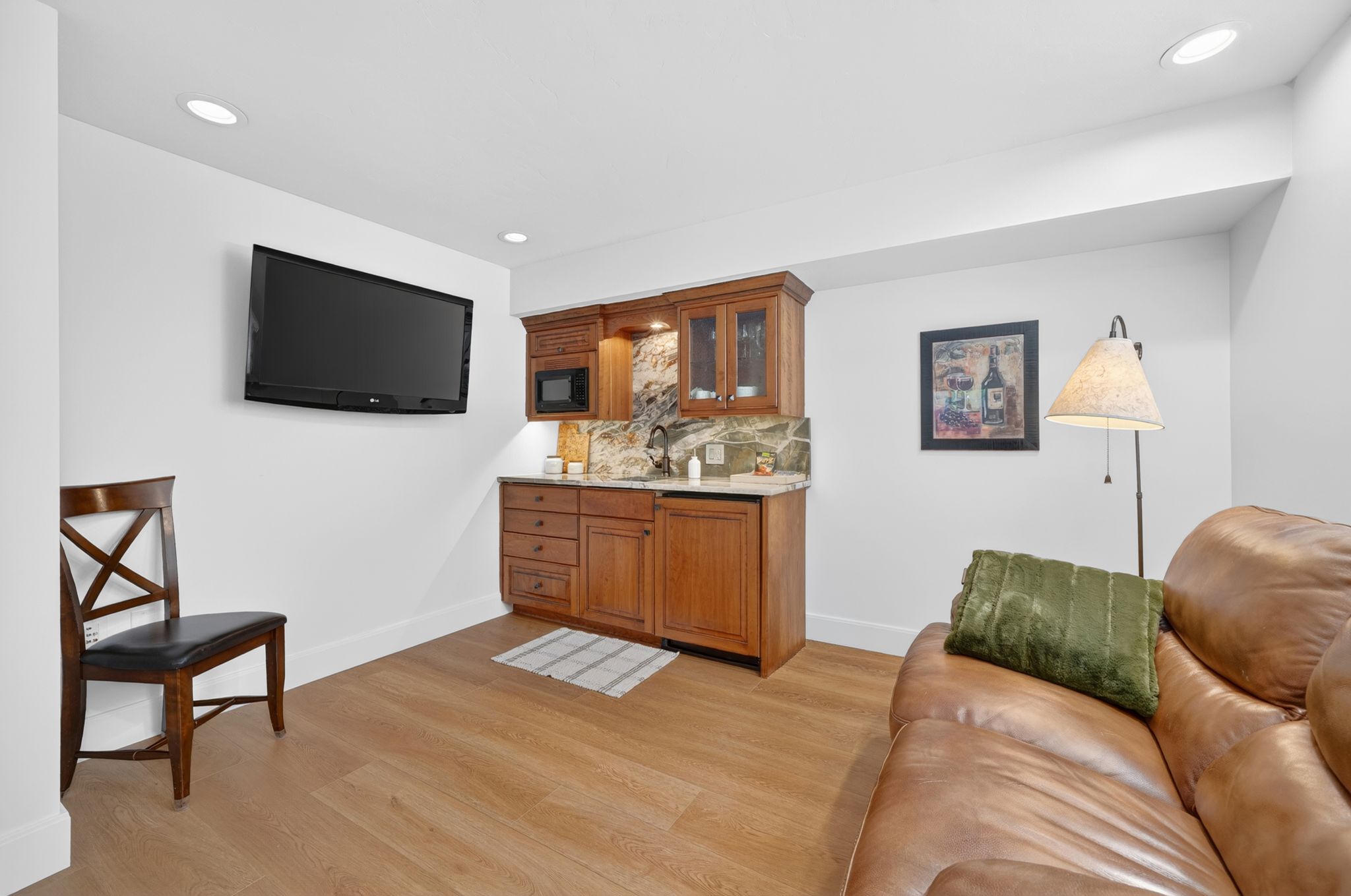 Built-in wet bar featuring wood-finish cabinetry, under-cabinet lighting, and stone backsplash