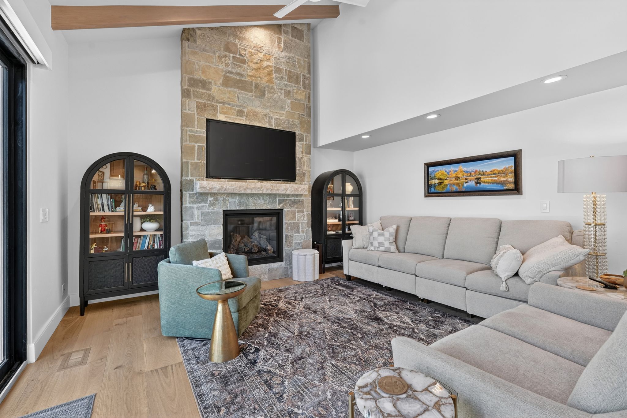 Spacious living area featuring a floor-to-ceiling stone fireplace, vaulted ceilings with an exposed wood beam, recessed lighting, and light wood-finish flooring