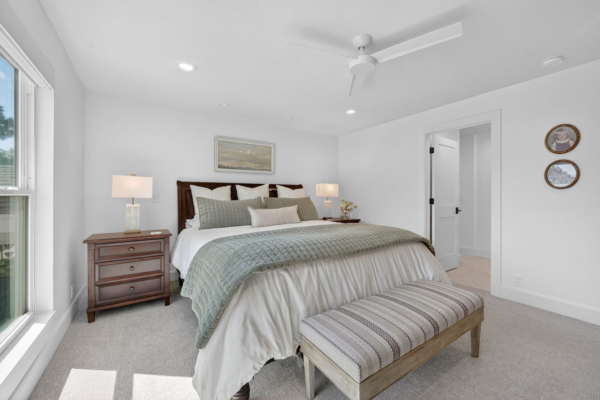Primary bedroom featuring neutral carpet flooring, recessed lighting, a white ceiling fan, and a large window with white trim and automatic shades
