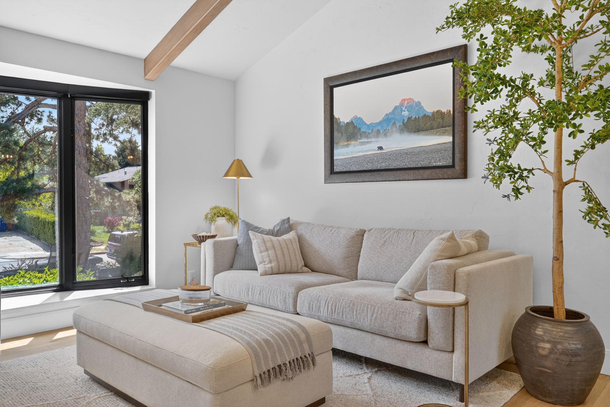Vaulted ceiling with exposed wood beam, large black-framed window, light wood-finish flooring, and white wall finishes