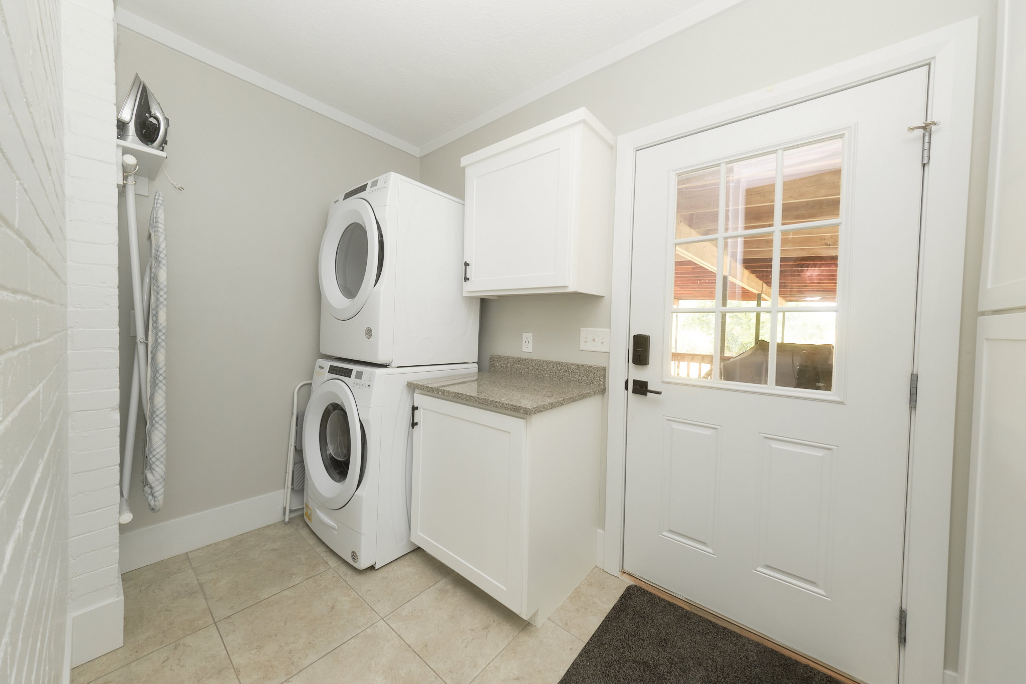 Dedicated laundry area featuring stacked appliances, built-in cabinetry, a stone-finish countertop, tiled flooring, and a glass-paned exterior door