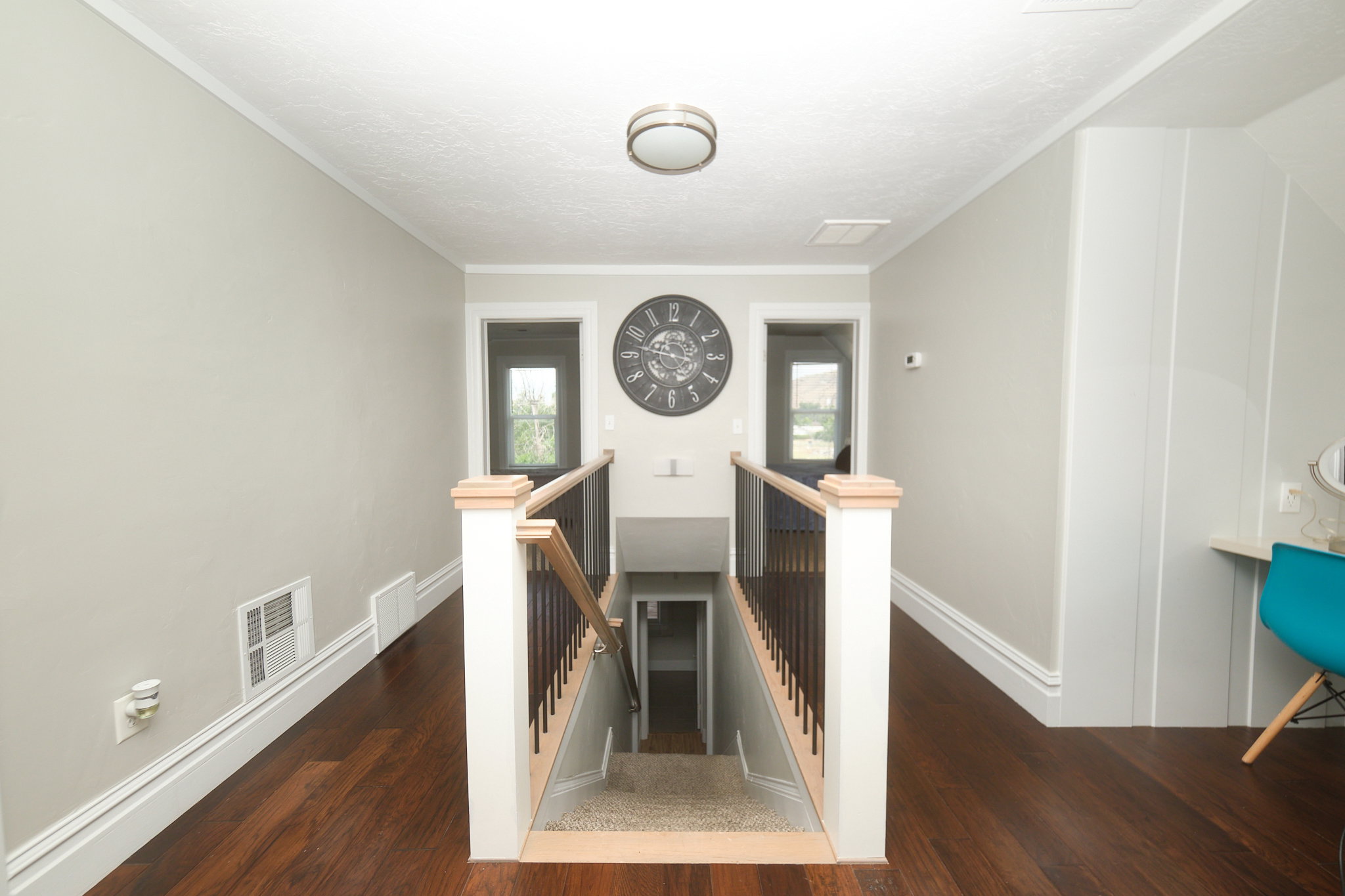 Upper-level landing featuring wood-finish flooring, a contemporary ceiling light fixture, and a staircase with light wood newel posts and dark balusters