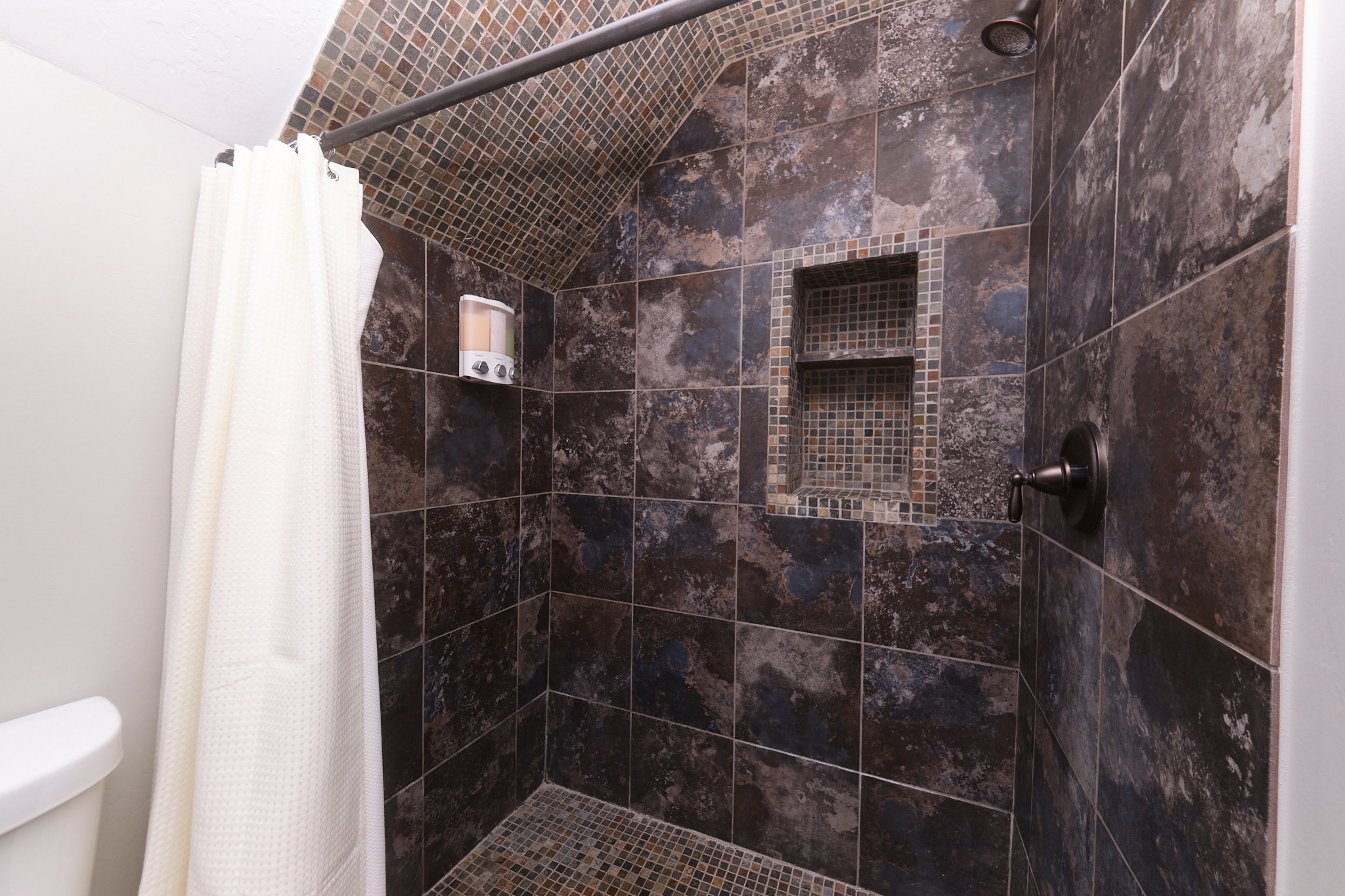 Shower enclosure featuring large format stone-look wall tiles, mosaic tile shower floor, and a recessed mosaic tile niche