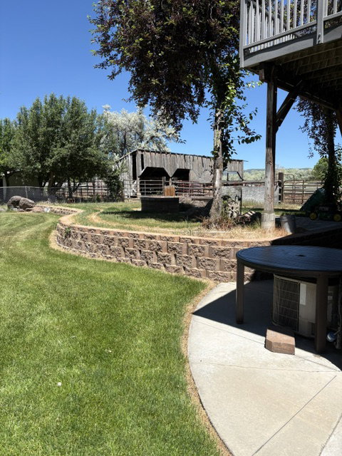Expansive backyard featuring a concrete patio, terraced lawn, and a decorative block retaining wall