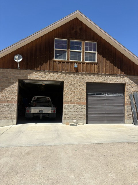 Two-story structure featuring a stone and brick veneer lower level with two garage doors, and a wood-paneled upper level with three windows