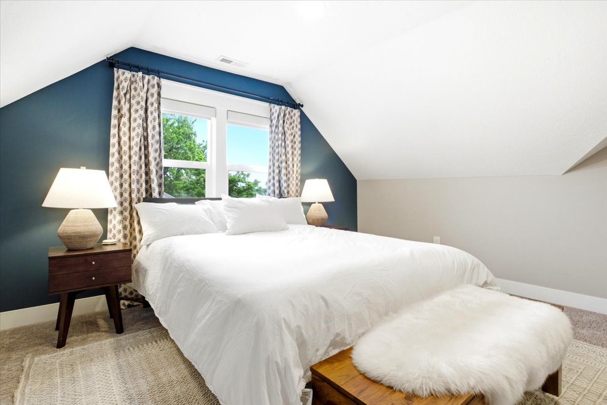 Attic space featuring a window with white trim, angled walls, a dark blue accent wall, and neutral carpet flooring