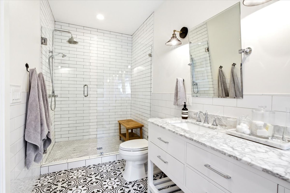 Bathroom featuring a glass-enclosed shower with subway tile surround, patterned floor tile, single vanity with a stone countertop, and an undermount sink