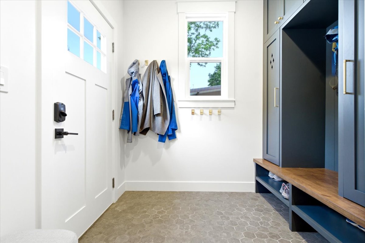 Entryway featuring hexagonal floor tiles, white paneled door with matte black hardware, built-in storage lockers in a deep blue finish, and a wood-finish bench with open shelving