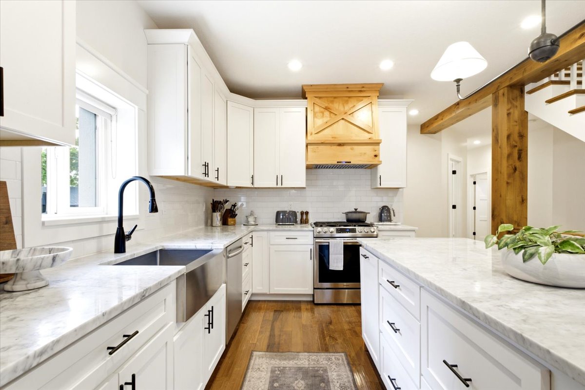 Bright kitchen featuring white shaker cabinetry, stainless steel appliances, a wood-finish range hood, stone countertops, and wood-finish flooring