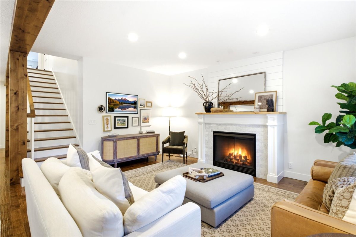 Living area featuring a fireplace with a white mantel and tile surround, wood-finish flooring, a shiplap accent wall, and recessed lighting