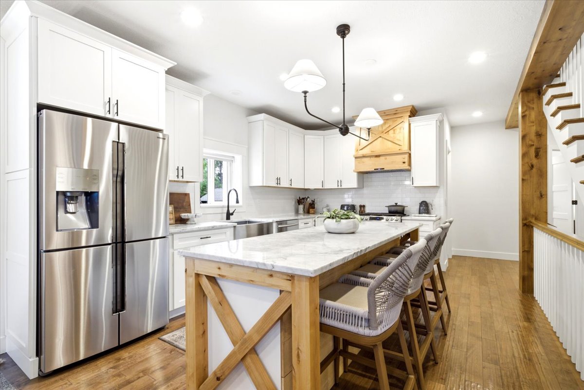 Kitchen featuring a substantial island with a stone countertop and wood-finish base, stainless steel refrigerator, white cabinetry, wood-finish flooring, and a decorative wood range hood