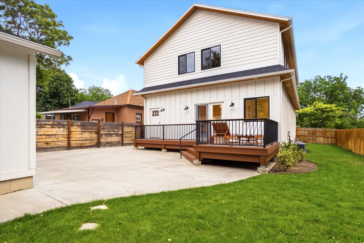 Contemporary white exterior with a wood-tone deck, black railings, and multiple exterior light fixtures