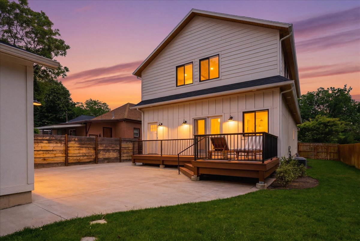 Rear exterior featuring a large elevated deck with dark railings, a concrete patio, and a grass lawn