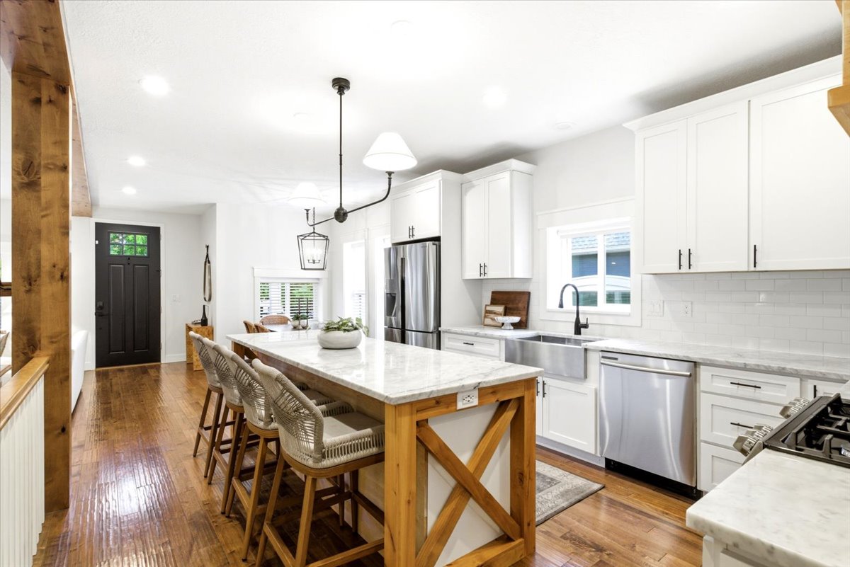 Bright kitchen featuring an expansive center island with seating, white shaker cabinetry, stainless steel appliances, a farmhouse sink, and wood-finish flooring